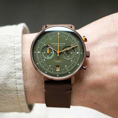 Herrklocka på handleden: grön urtavla, orange visare och brunt läderarmband