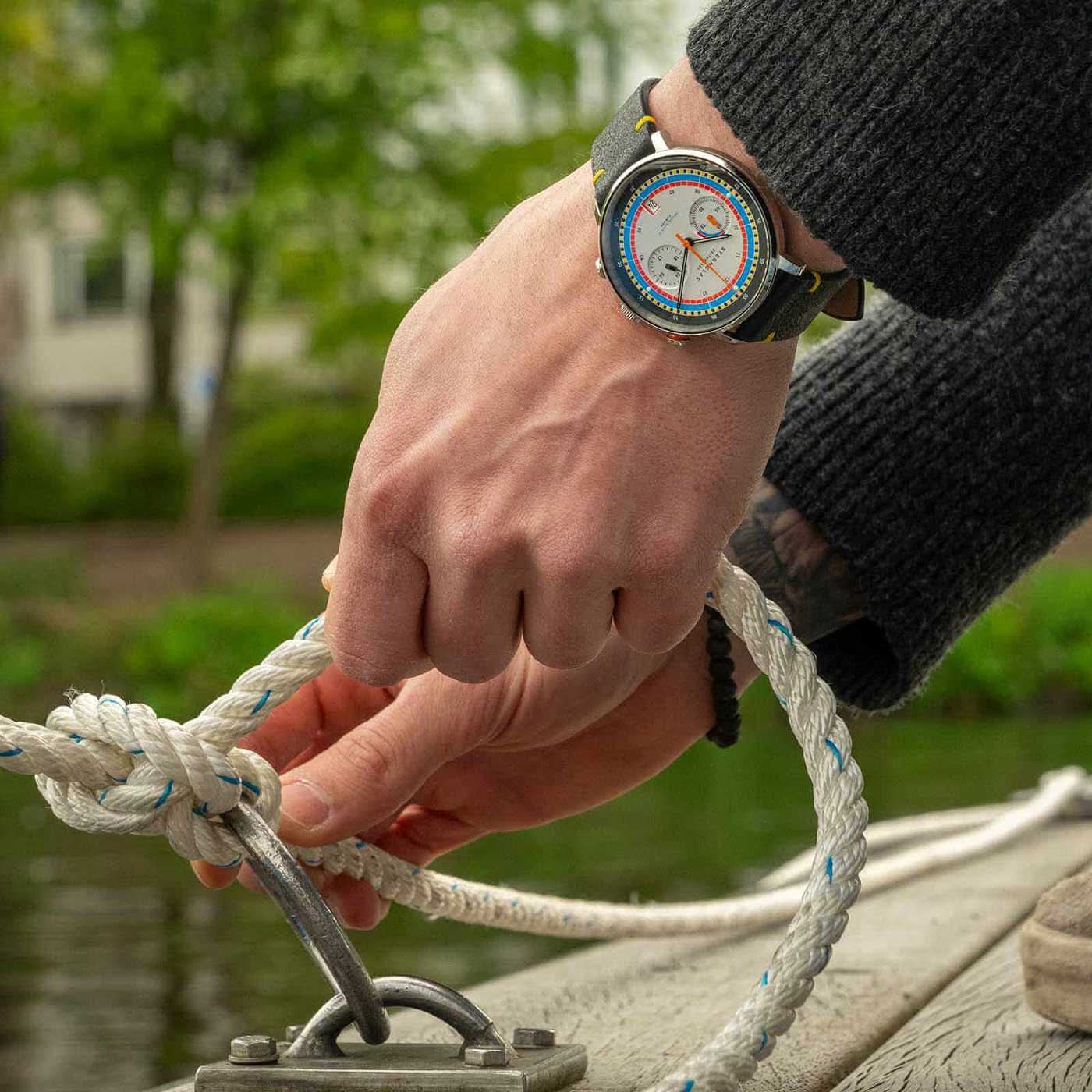 Herrklocka på handleden: svart läderarmband, silverfärgad urtavla med färgglada markeringar