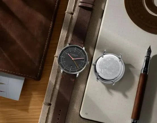 Herrklocka med brunt läderarmband på underlag, svart rund urtavla