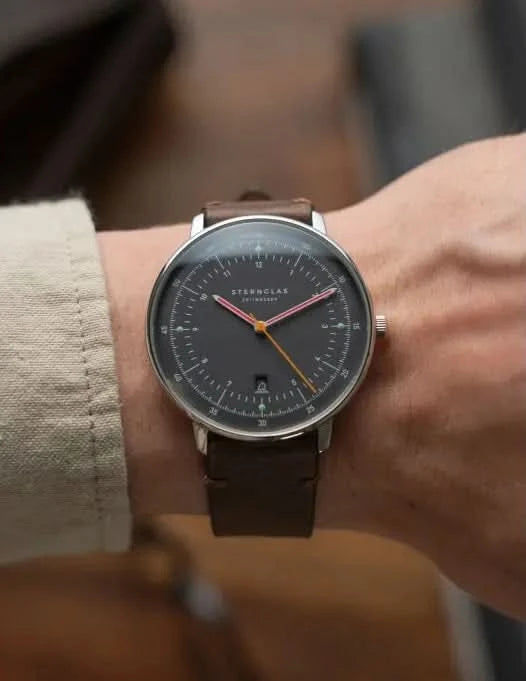Herrklocka på handleden med brunt läderarmband och svart urtavla