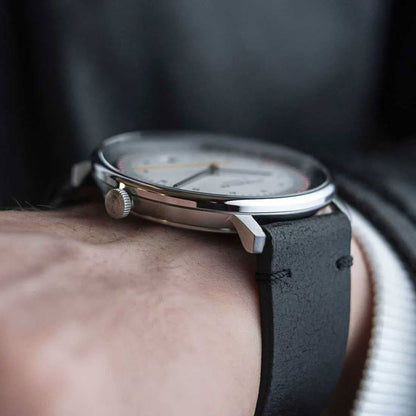 Herrklocka på handleden: svart läderarmband, silverfärgat boett och krona.
