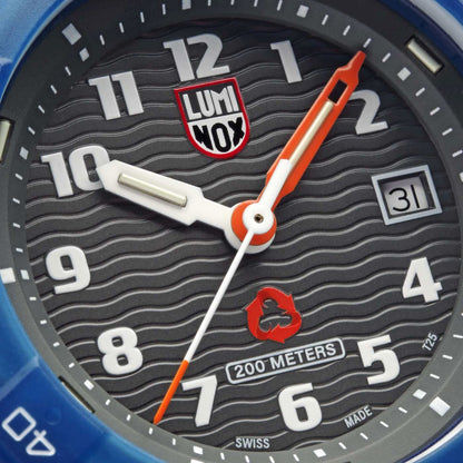 Närbild på herrur: mörk urtavla med Luminox-logotyp, orangea visare och datumvisning.