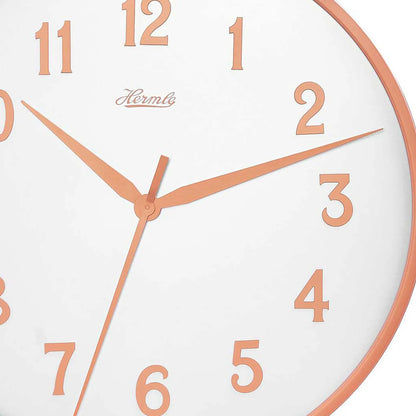 Detaljerad vy av väggklockan: vit urtavla med orange siffror, visare och Hermle-logotyp