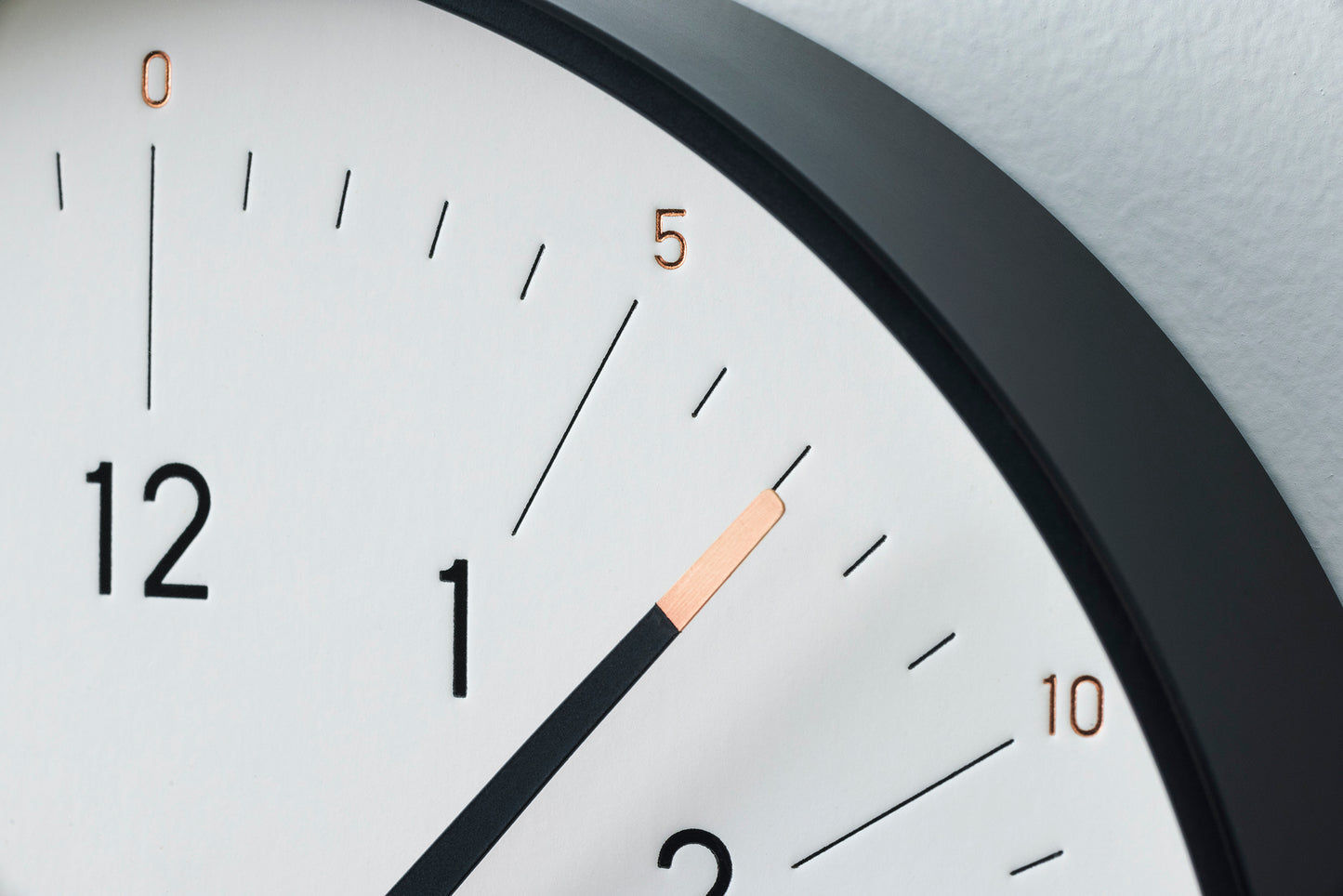 Detail vom weißen Zifferblatt der Wanduhr: schwarze Einfassung, Stundenzeiger.