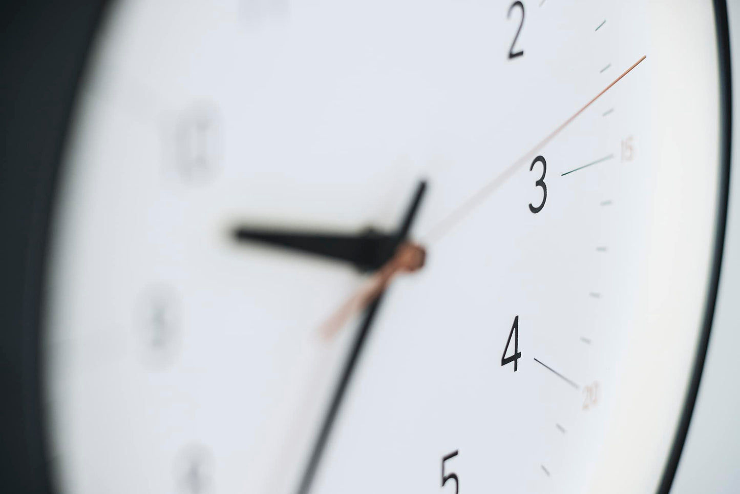 Nahaufnahme der Uhrzeiger auf dem weißen Zifferblatt der Wanduhr mit schwarzem Rand.