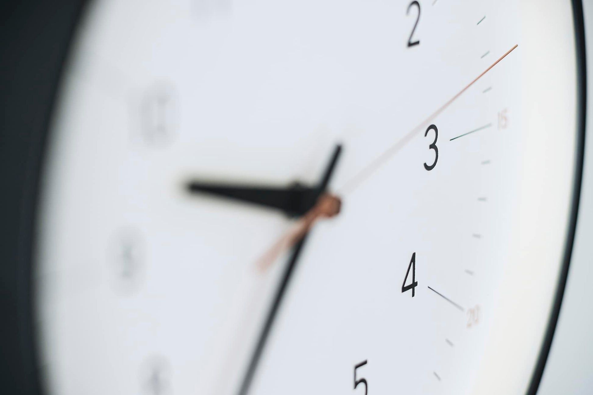 Nahaufnahme der Uhrzeiger auf dem weißen Zifferblatt der Wanduhr mit schwarzem Rand.