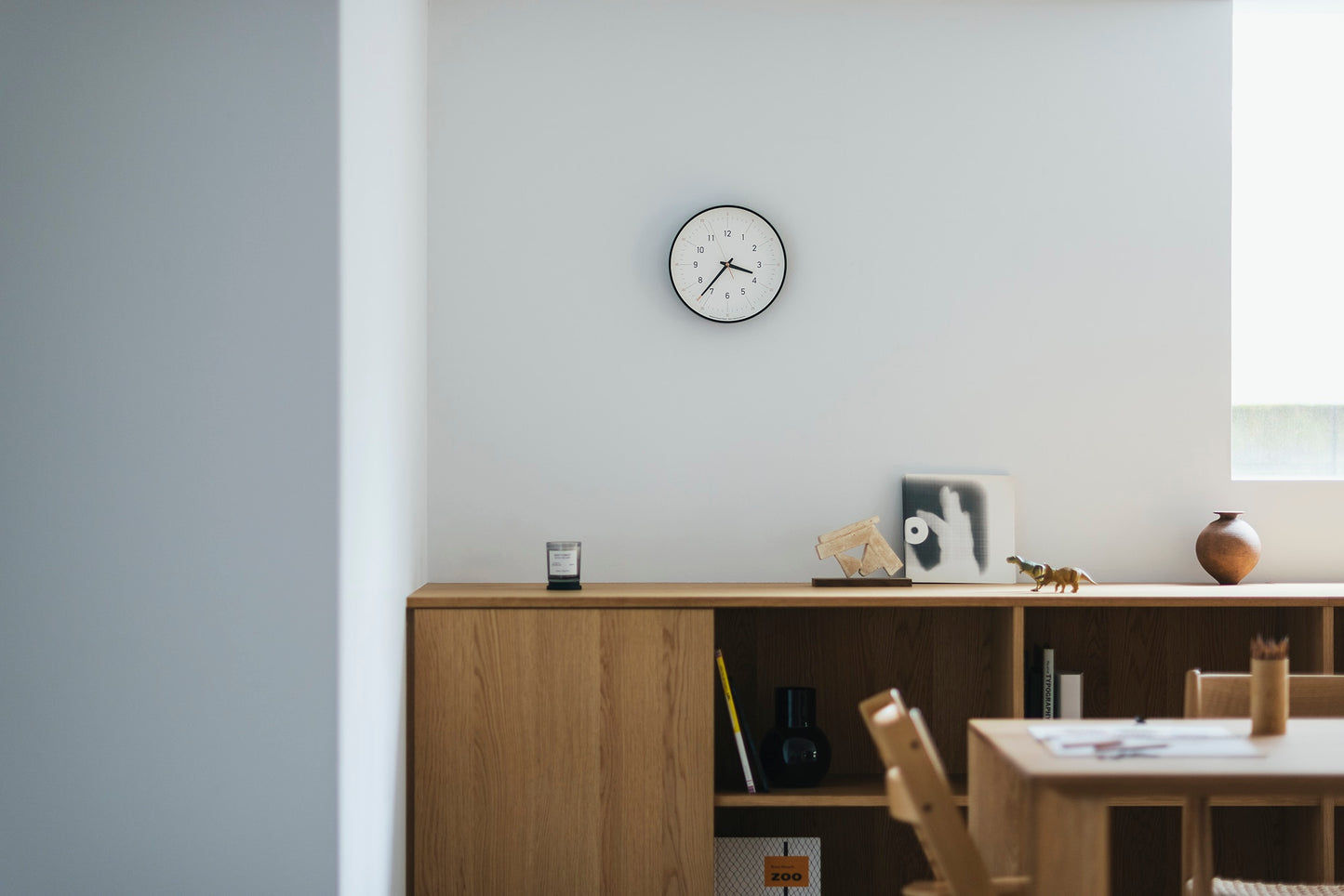 Weiße Wanduhr an der Wand mit kleinem Rundzifferblatt und schwarzem Rahmen.