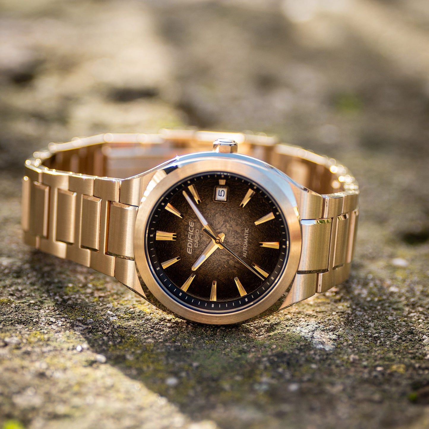 Casio Edifice Uhr in Seitenansicht auf Steinen, goldfarbenes Metallband, schwarzes Zifferblatt