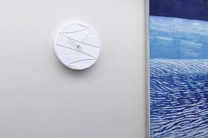 Weiße Wanduhr an der Wand mit abstrakten Linien und schlanken Zeigern