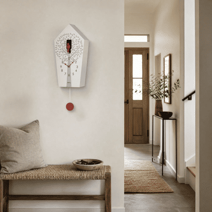 Wanduhr mit weißem Kuckucks-Gehäuse und rotem Pendelknopf an der Wand