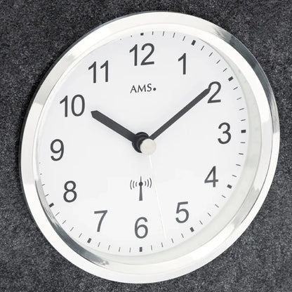 Nahaufnahme: rundes Zifferblatt mit AMS-Schrift und Funkwellen-Symbol, schwarze Zeiger.