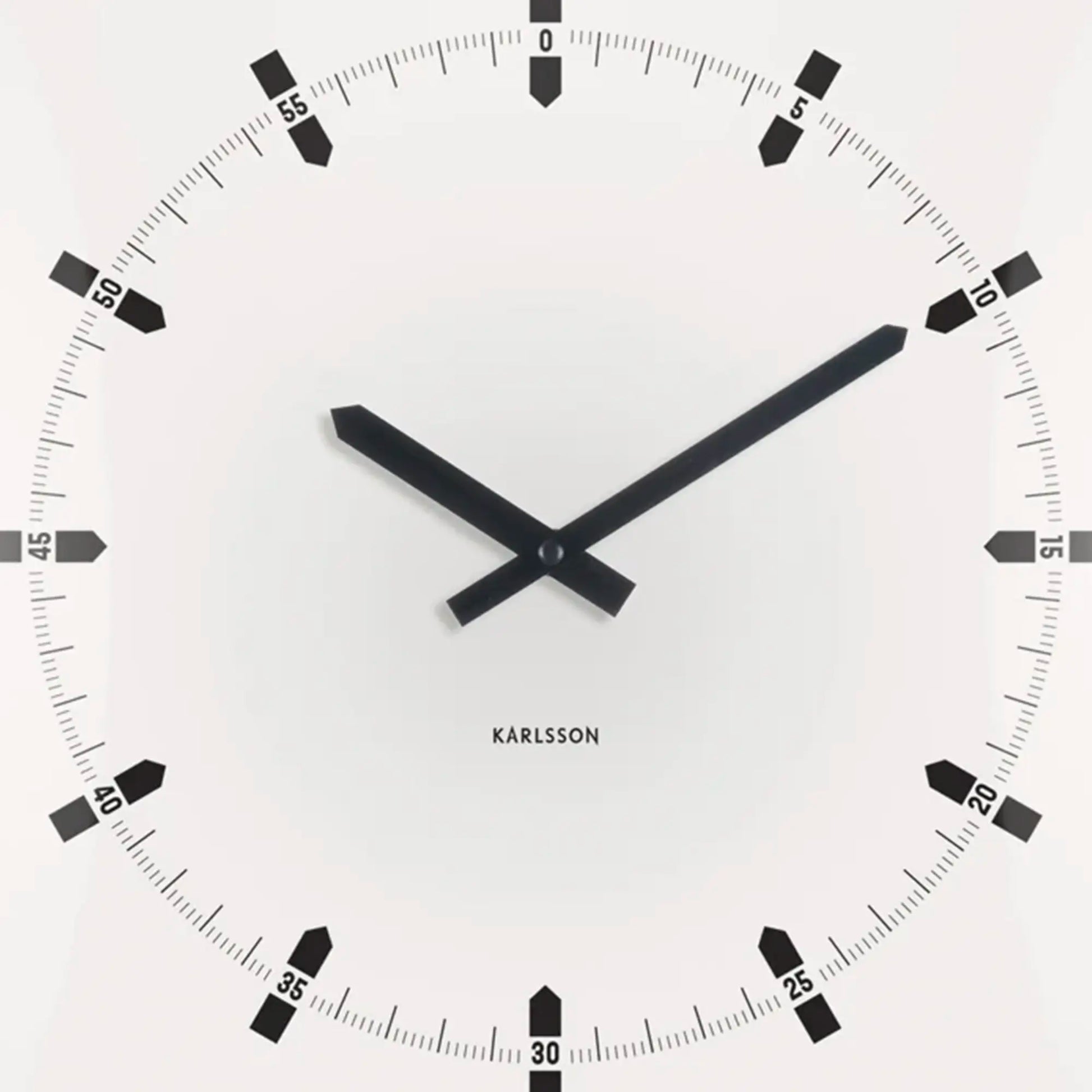 Nahaufnahme der quadratischen Wanduhr: weißes Zifferblatt, schwarze Zeiger und Minutenmarken.