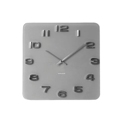 Vorderansicht: quadratische graue Wanduhr mit offenem Zifferblatt und Metallzeigern