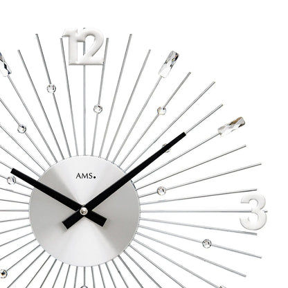 Nahaufnahme: silberne Wanduhr mit Metallstäben, schwarzen Zeigern und Ziffer 12