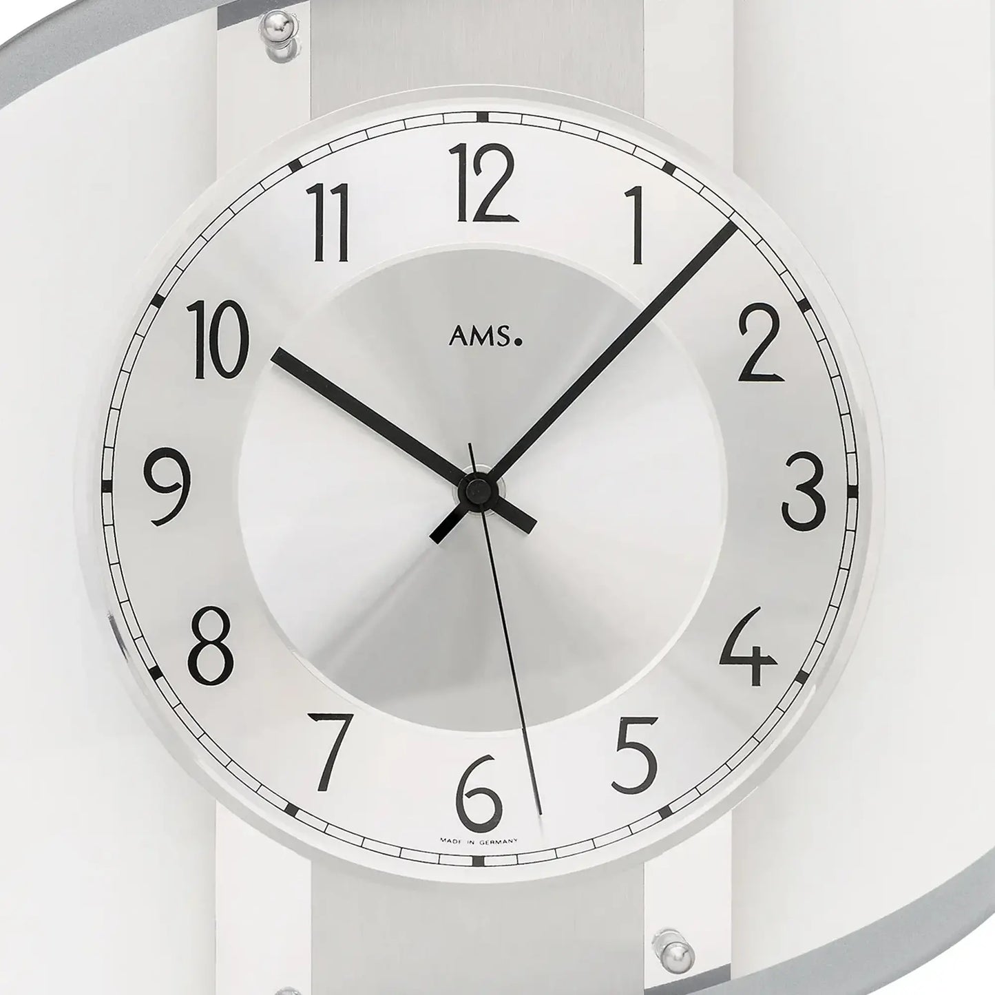 Nahaufnahme Wanduhr: weißes Zifferblatt mit AMS-Logo, schwarze Zeiger, Facettenring