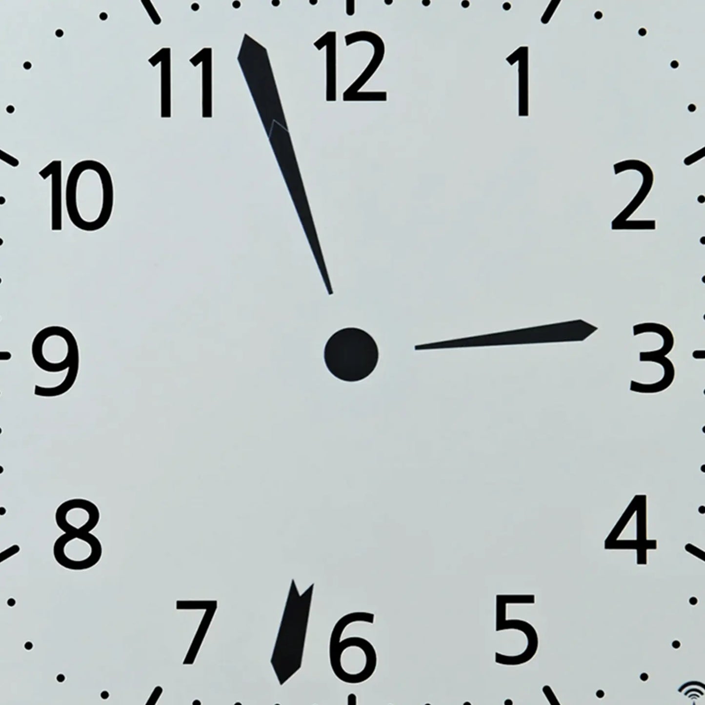 Nahaufnahme der weißen Funk-Wanduhr: schwarze Zeiger, Punkte als Minutenmarken, Ziffern 1–12.