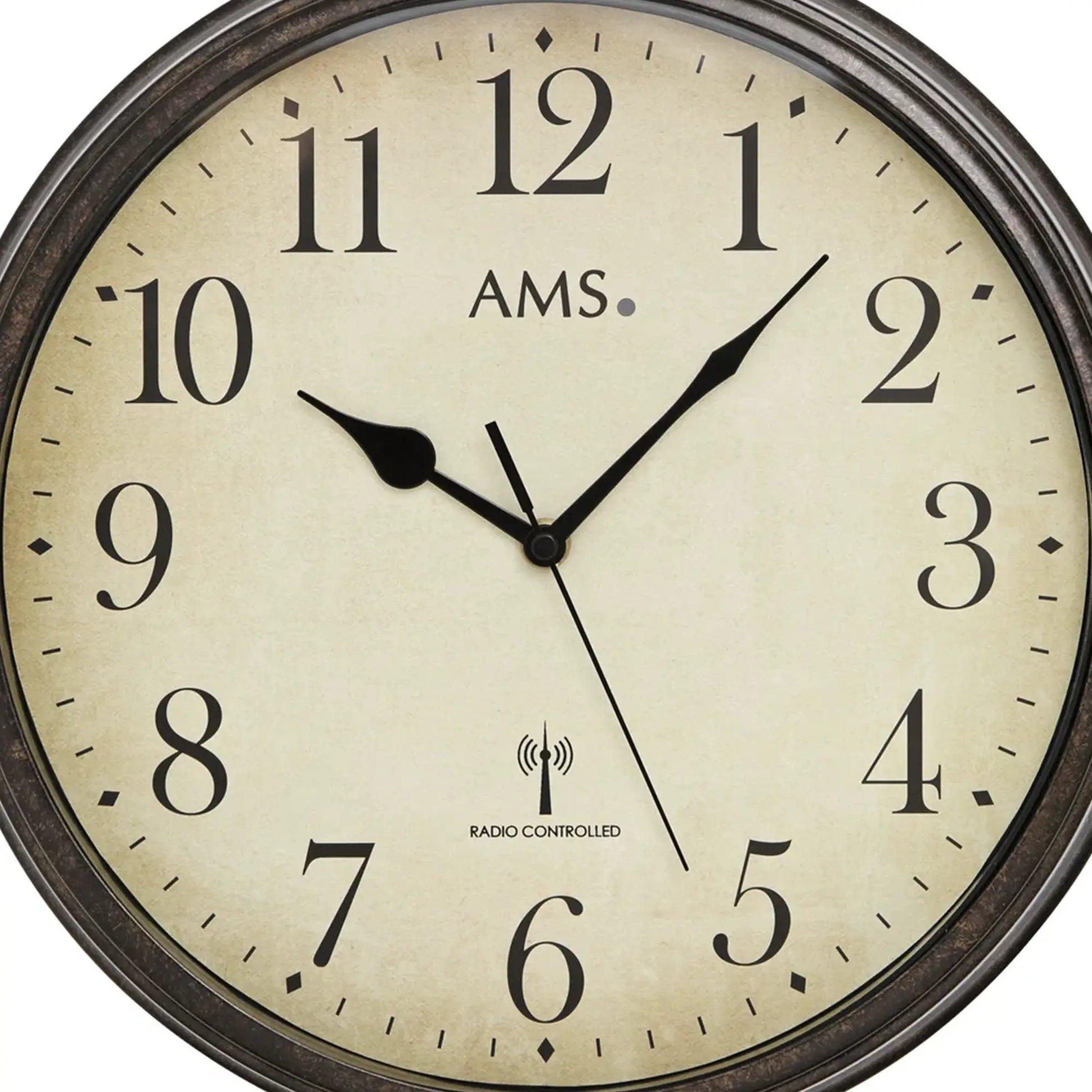 Nahaufnahme: AMS Wanduhr mit beigem Zifferblatt, schwarzen Zeigern und Funk-Logo