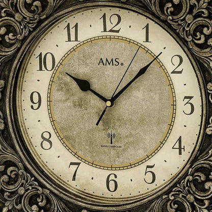 Nahaufnahme der Funk-Wanduhr: Ziffernblatt mit AMS-Logo, goldenem Ring und schwarzen Zeigern