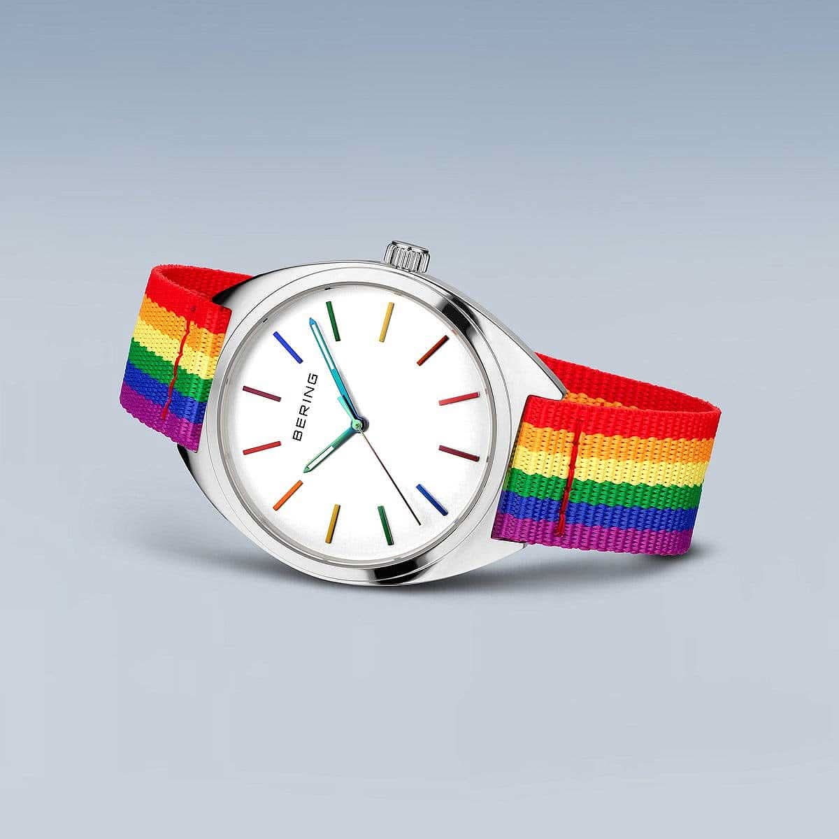 "Reloj redondo con esfera blanca, índices de colores y correa textil de arcoíris"