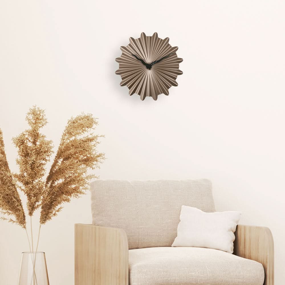 Reloj de pared con aspecto de concha, acabado metálico dorado sobre pared clara