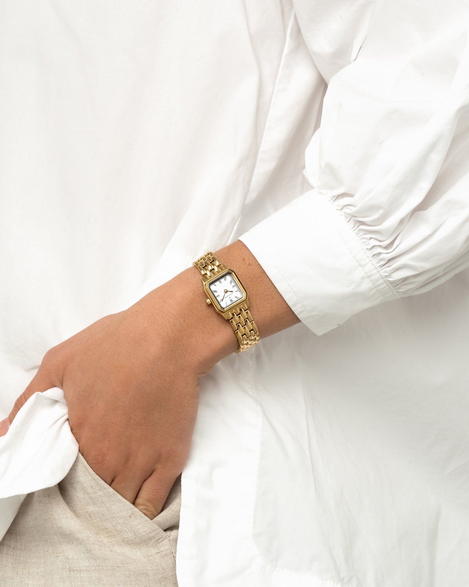 Goldene Damenarmbanduhr am Handgelenk mit rechteckigem Gehäuse und weißem Zifferblatt