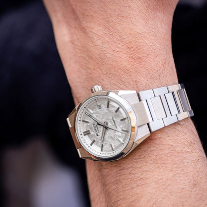 Seitenansicht: silberne Herrenarmbanduhr mit hellem Zifferblatt und Datumsanzeige bei 5