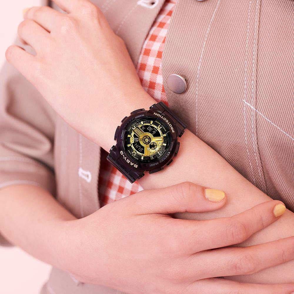 "Reloj de mujer en detalle: pulsera negra con bisel dorado en la muñeca"