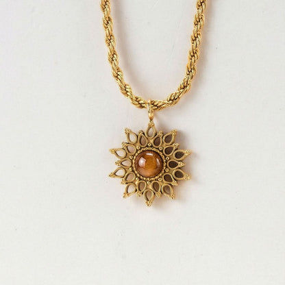 Collar con cadena dorada y colgante de sol con piedra marrón sobre fondo claro