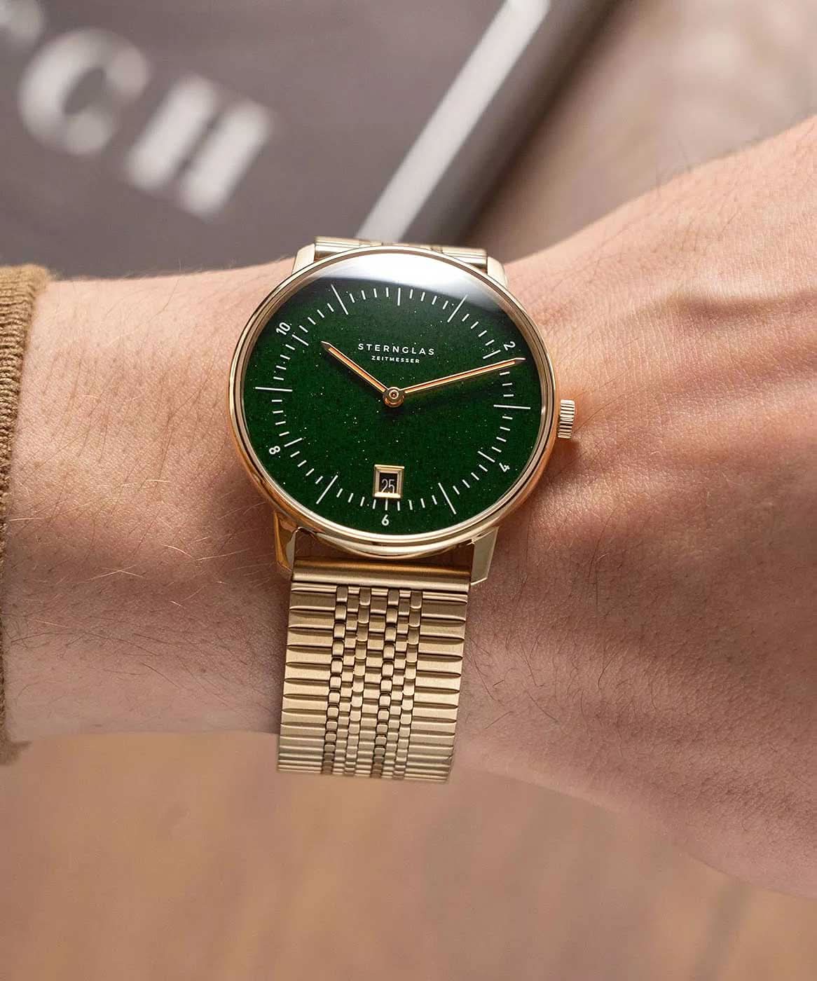 Reloj de hombre en la muñeca: correa de metal dorada, esfera verde con fecha