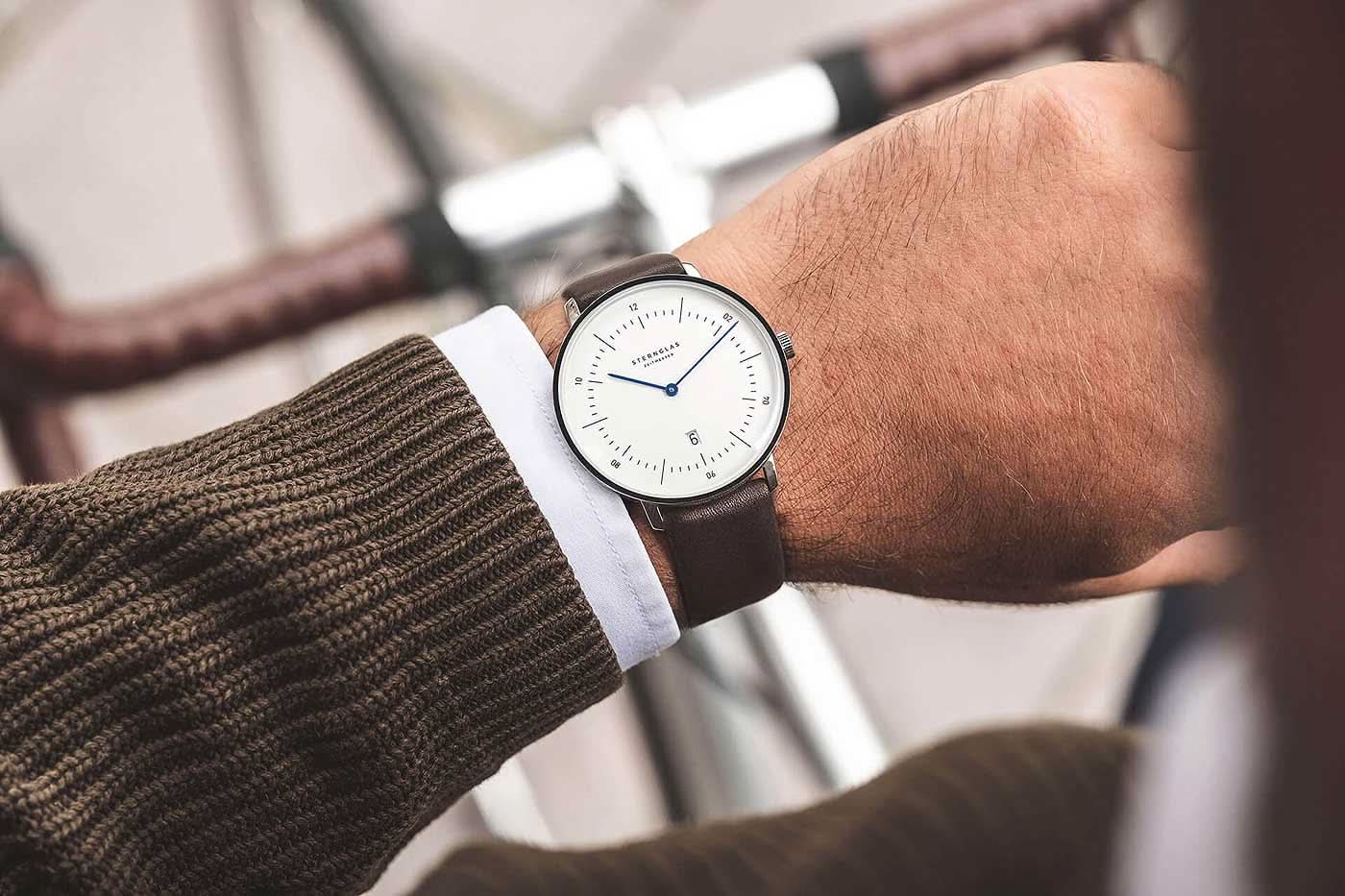 "Reloj de mujer en la muñeca con correa de cuero marrón y esfera redonda blanca"