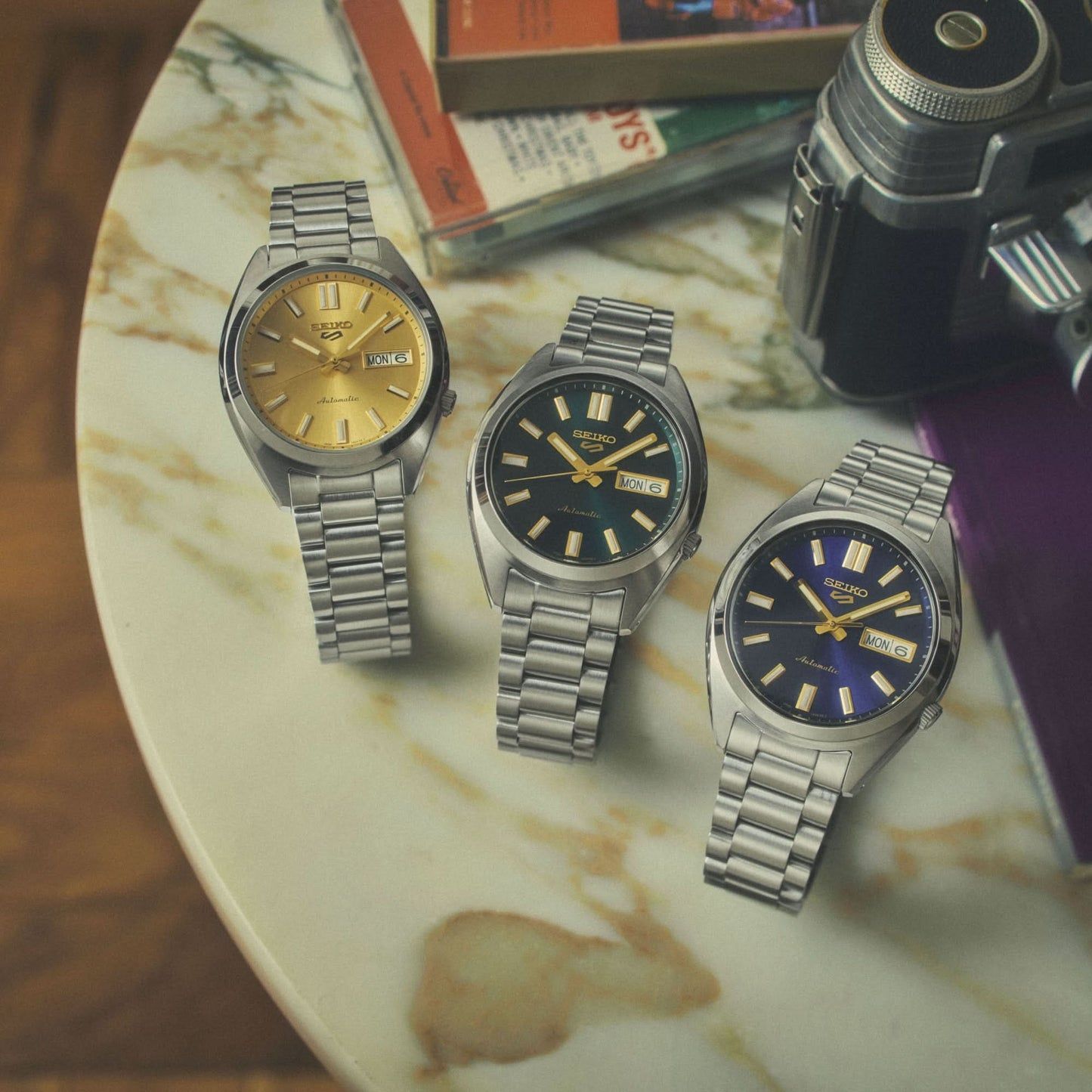 Tres relojes Seiko 5 Sports para hombre con esfera azul y brazalete de metal sobre una losa de piedra.