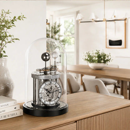 Reloj de mesa con campana de cristal sobre consola de madera, esfera plateada con números romanos