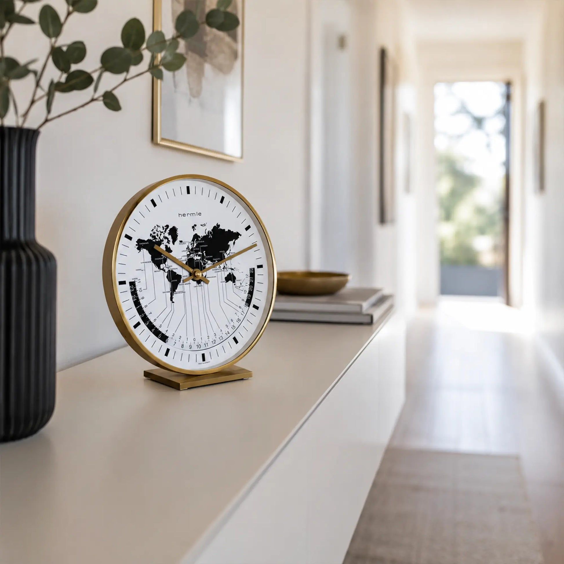 Reloj de mesa sobre consola blanca: borde de latón, mapa del mundo en la esfera, manecillas doradas