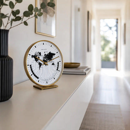 Reloj de mesa sobre consola blanca: borde de latón, mapa del mundo en la esfera, manecillas doradas
