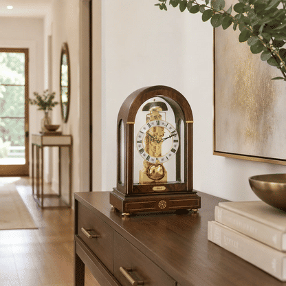 Reloj de mesa de madera sobre mueble, marco de cristal y esfera dorada con números romanos