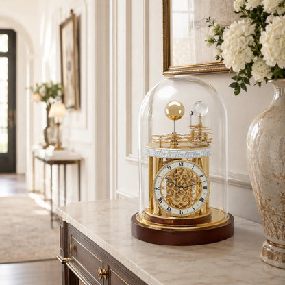 Reloj de mesa bajo campana de cristal sobre aparador claro, mecanismo dorado y base marrón