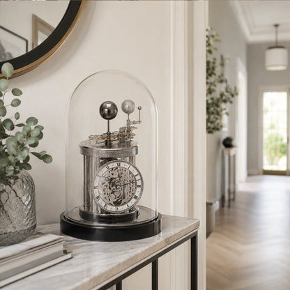 Reloj de mesa con campana de cristal, esfera plateada y base negra sobre tablero