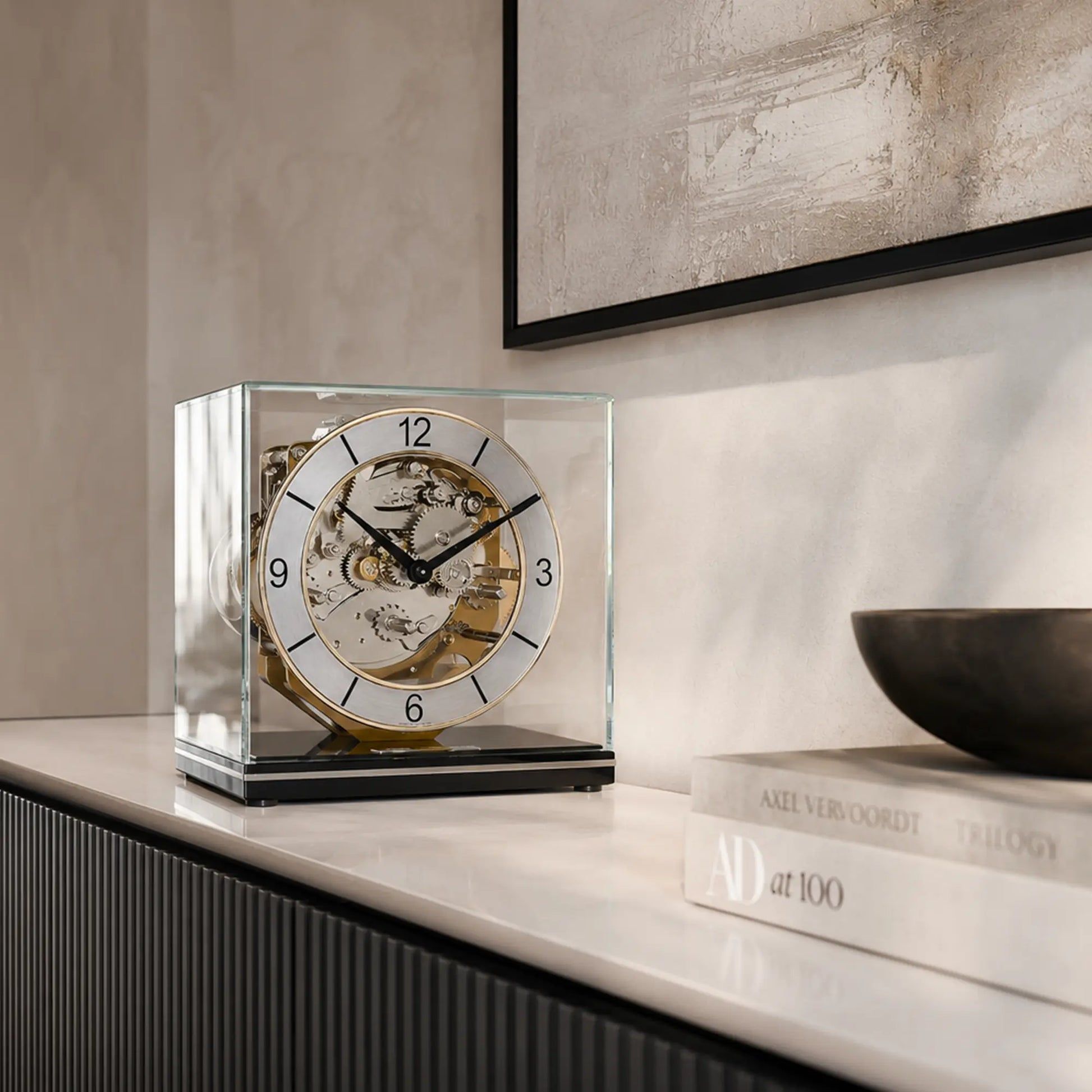 Reloj de mesa en caja de cristal con mecanismo mecánico visible, esfera redonda y números romanos