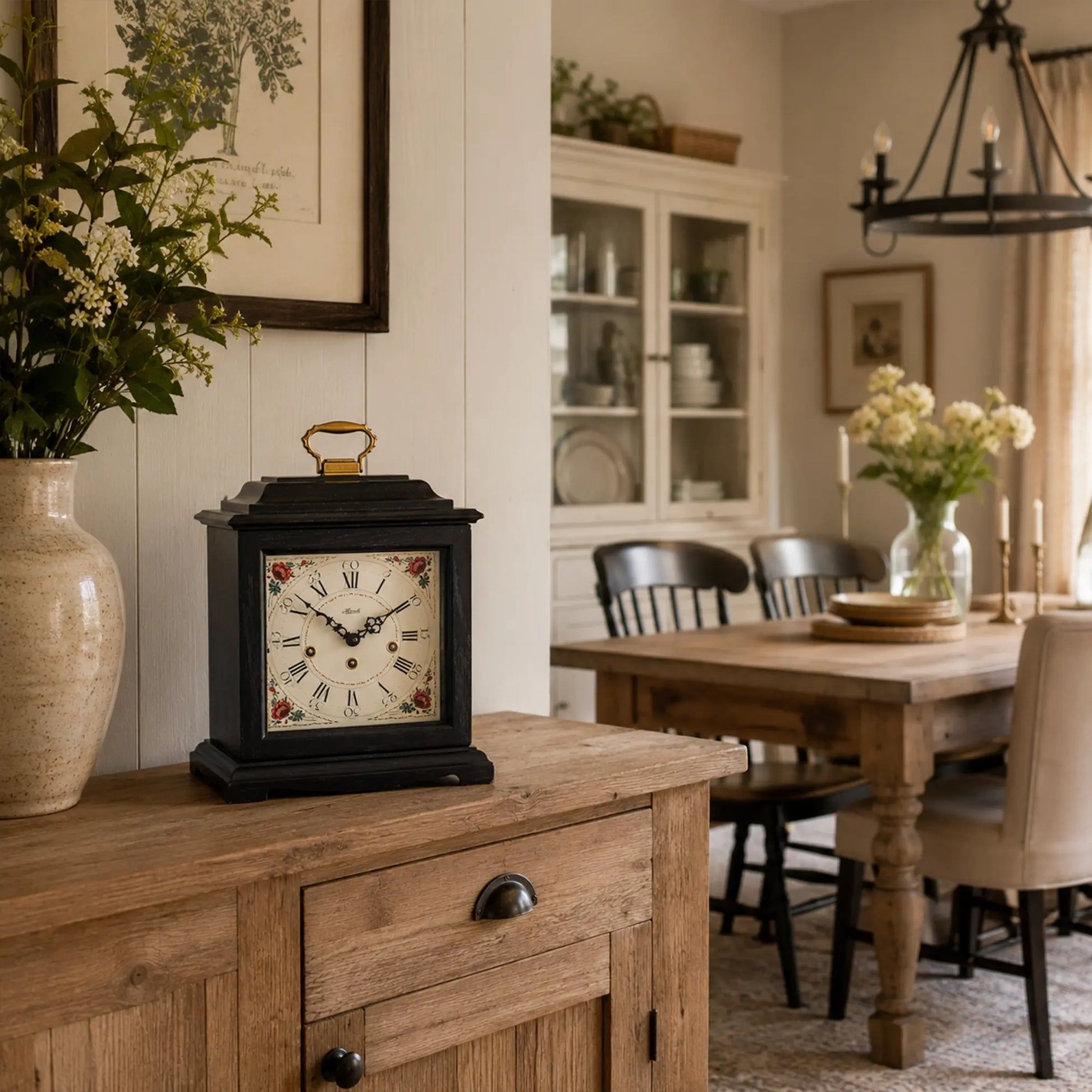 Reloj de mesa negro sobre aparador de madera con esfera floral y asa dorada