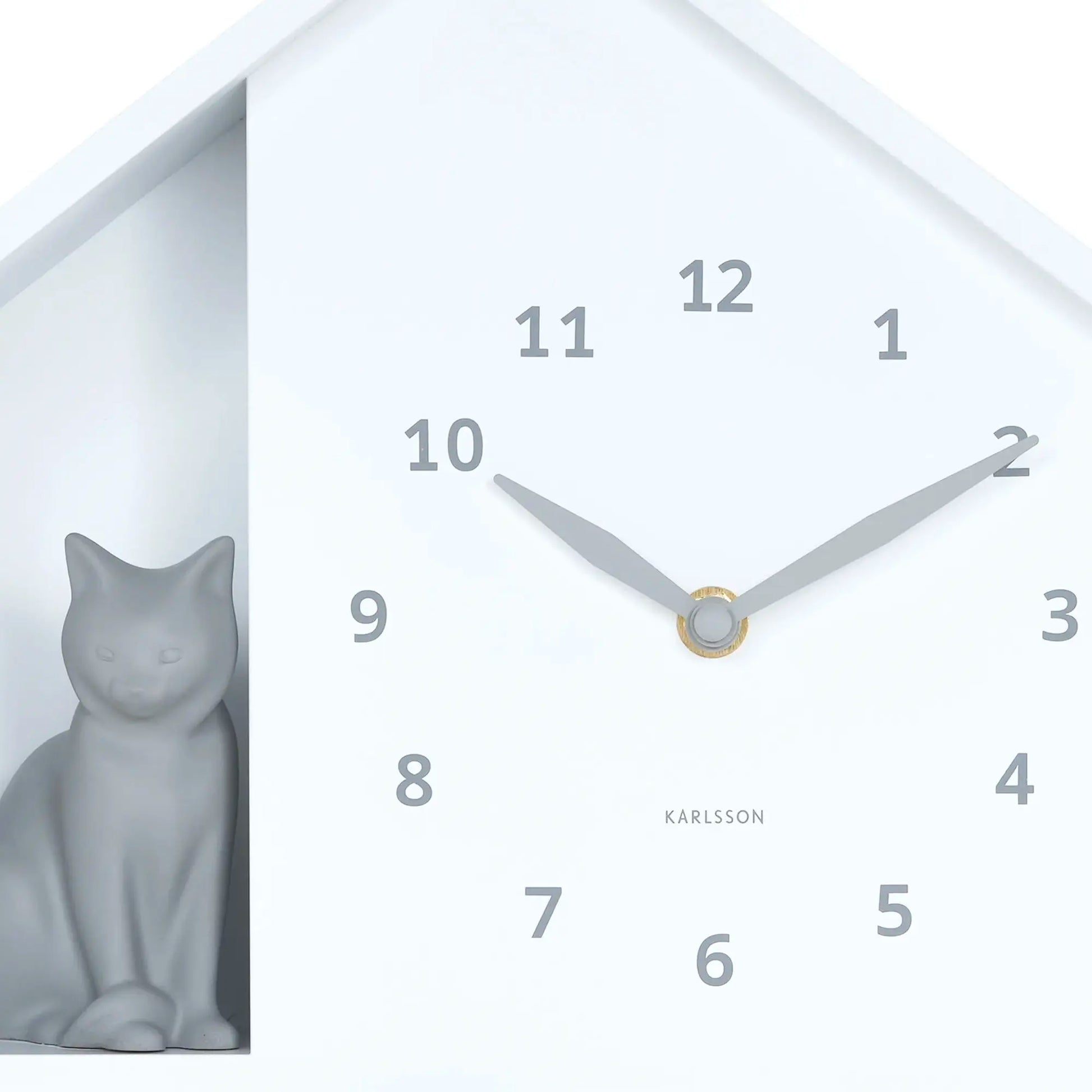 Nahansicht der weißen Wanduhr: Zeiger, Ziffern 1–12 und Katzenfigur im Fenster