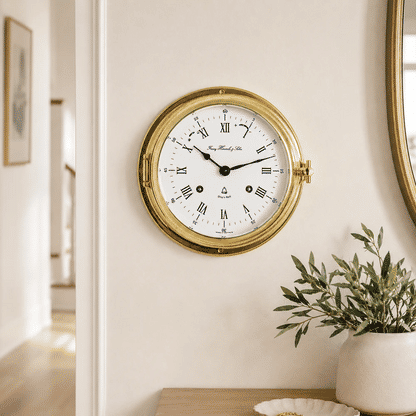 Reloj de pared redondo con anillo de latón y esfera blanca, manecillas azules y números romanos.