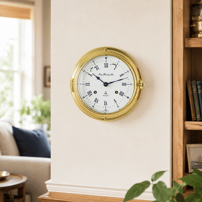 Reloj de pared con caja redonda de latón, esfera blanca y manecillas azules, marcadores romanos.