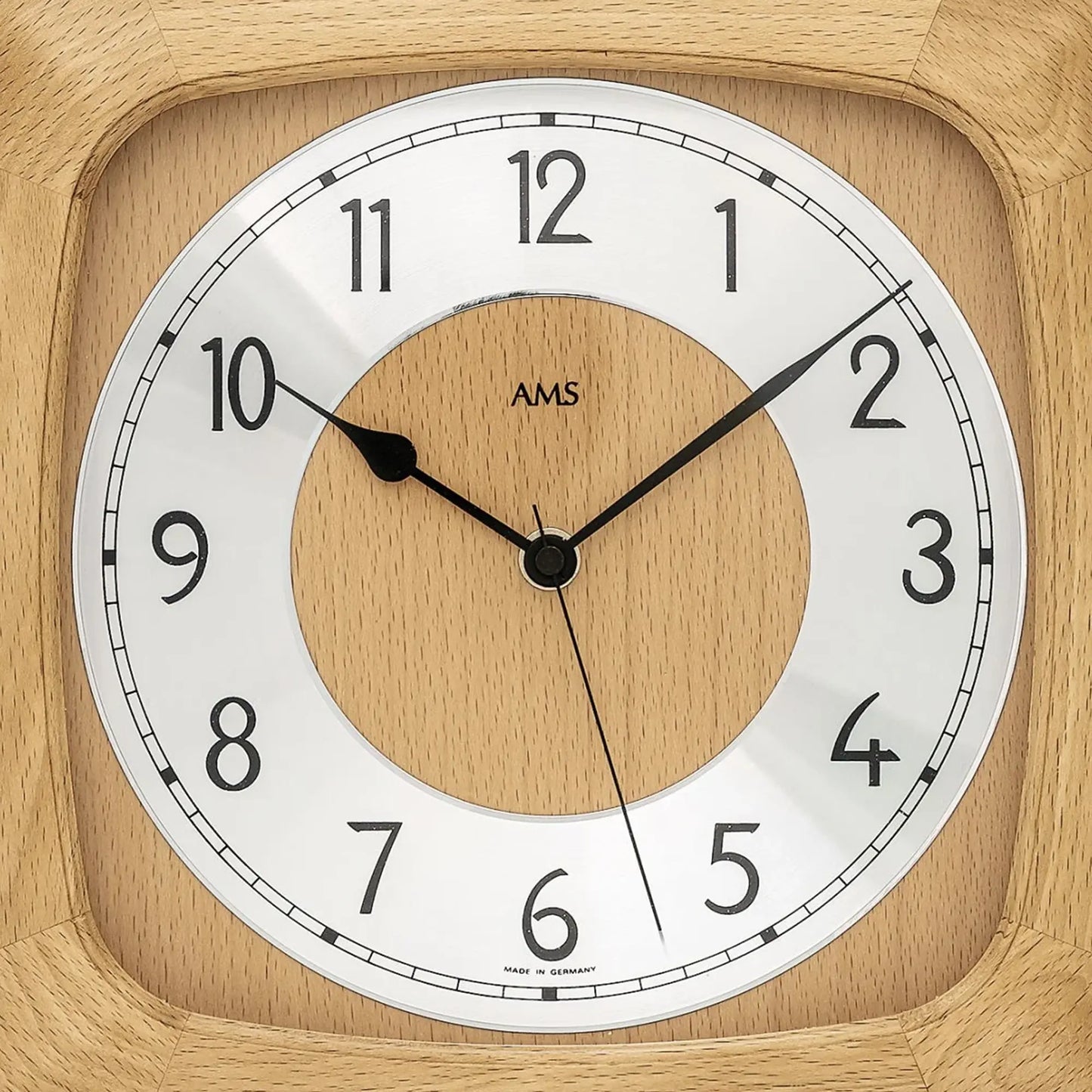 Nahaufnahme der Holz-Wanduhr: rundes Holz-Zifferblatt, schwarze Zeiger, AMS-Logo im Zentrum