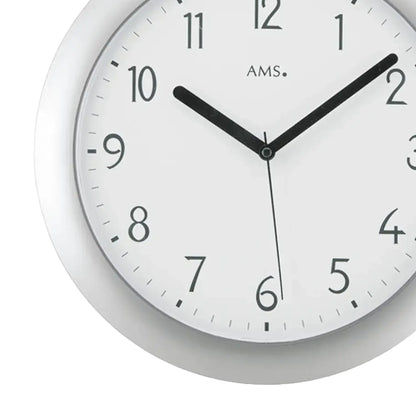 Nahaufnahme Funk-Wanduhr: silbernes Gehäuse, weißes Zifferblatt, schwarze Zeiger, AMS-Logo.