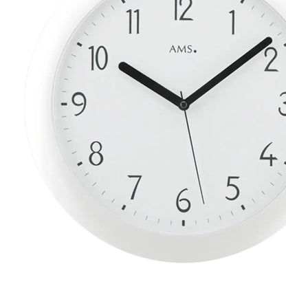 Nahaufnahme einer weißen Wanduhr mit schwarzen Zeigern und AMS-Markierung im Zifferblatt.