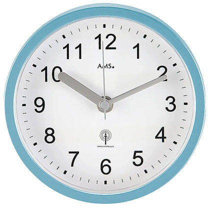 Nahaufnahme: Badezimmer-Wanduhr mit türkisfarbenem Rand, weißem Ziffernblatt, AMS-Logo.