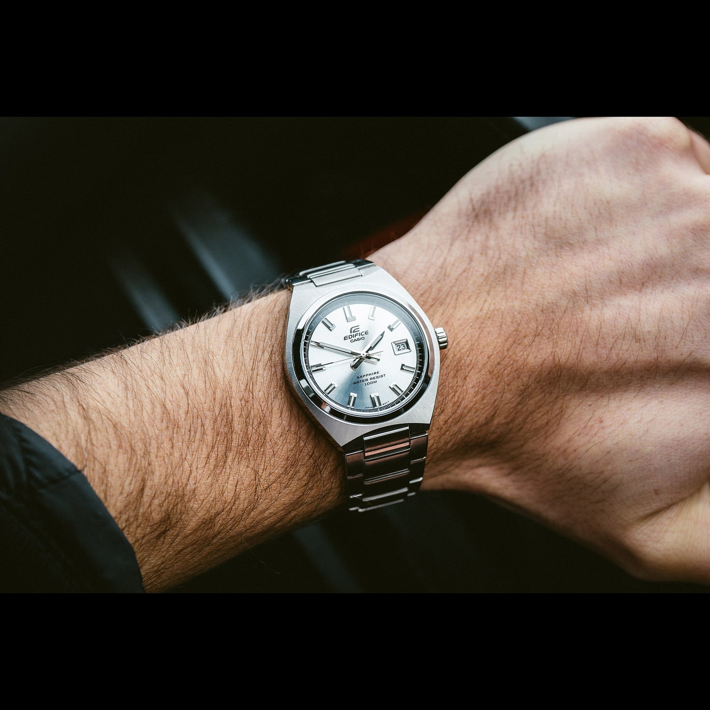 Silberne Herrenarmbanduhr am Handgelenk mit rundem Zifferblatt und Metallarmband