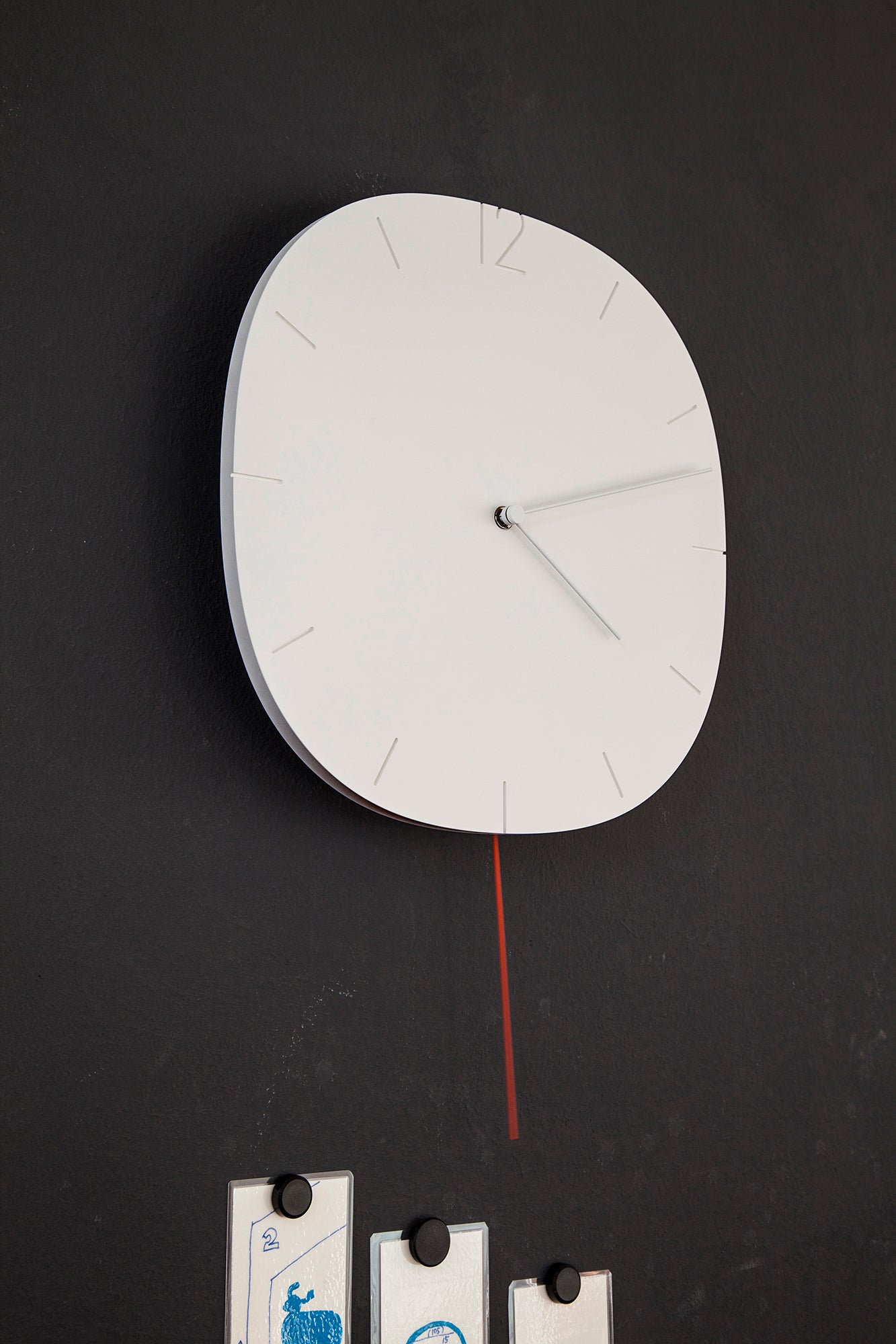 Weiße runde Wanduhr mit Zeigern und rotem Pendelstreifen an der Wand