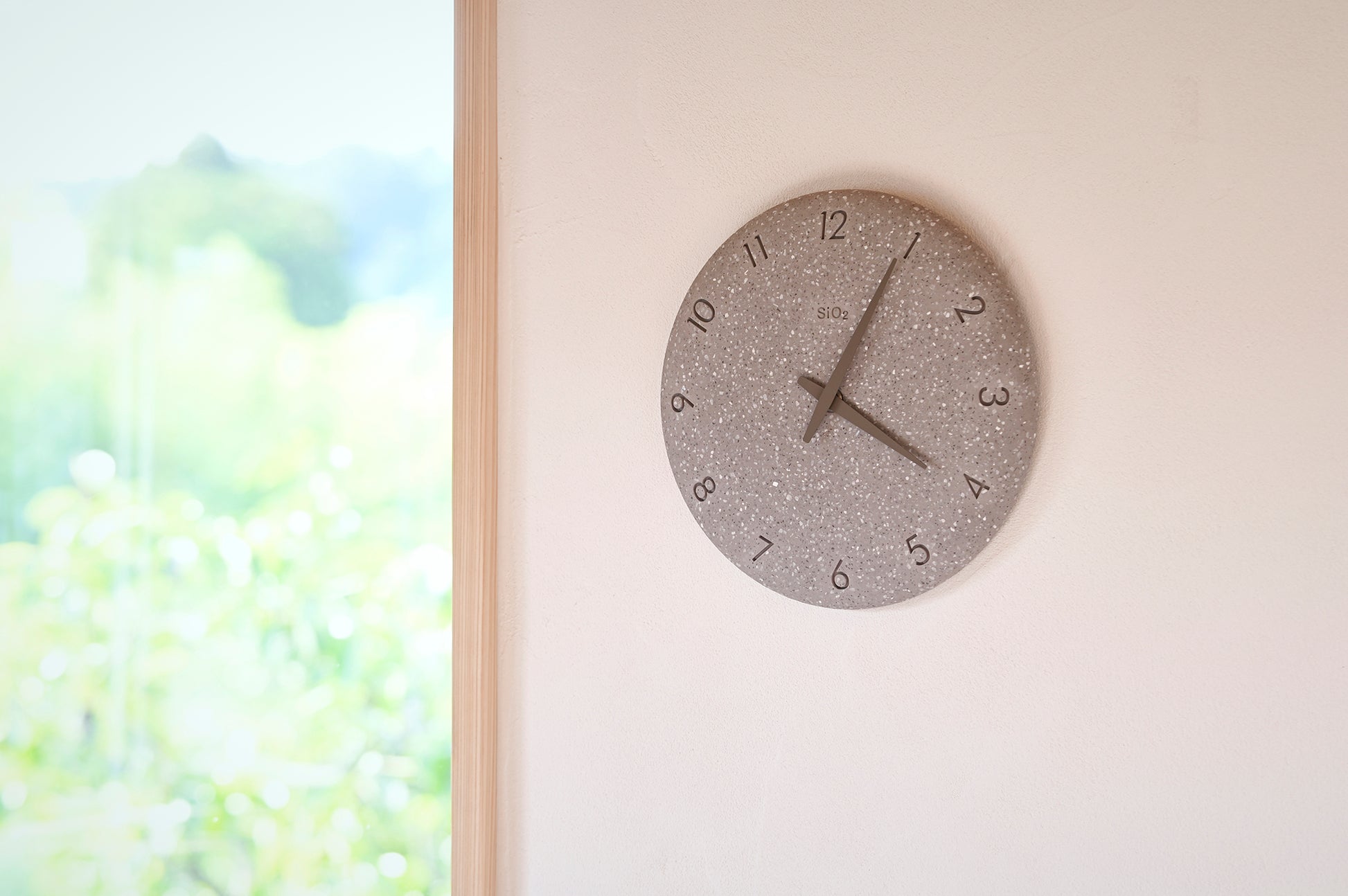 Kleine graue Wanduhr mit gesprenkeltem Stein-Look an heller Wand, Zeiger sichtbar