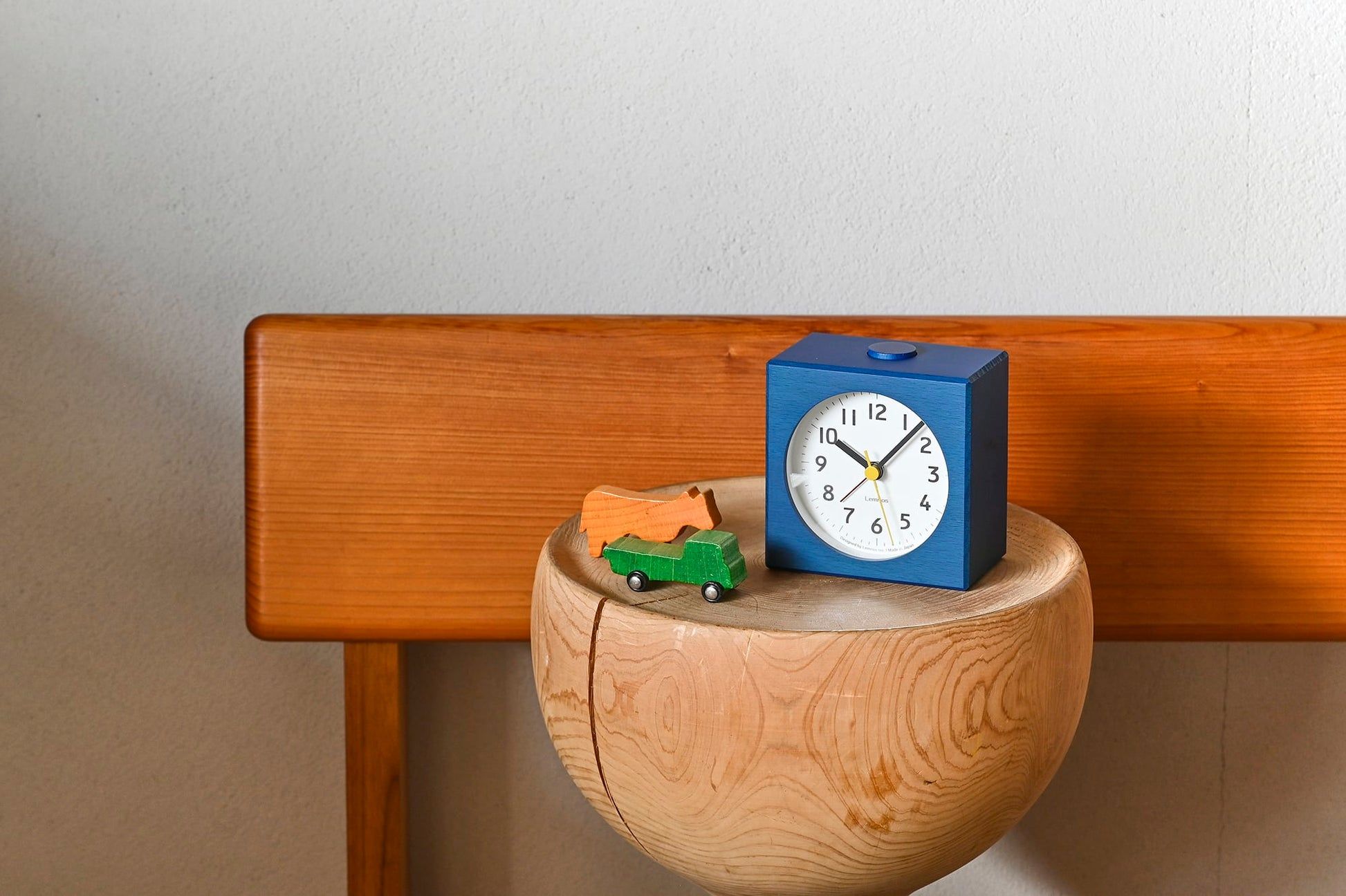 Elektronischer Wecker mit blauem Gehäuse auf Holzsockel, analoges Zifferblatt